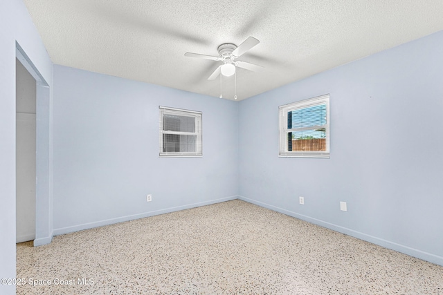 spare room featuring a ceiling fan, speckle patterned floor, baseboards, and a textured ceiling