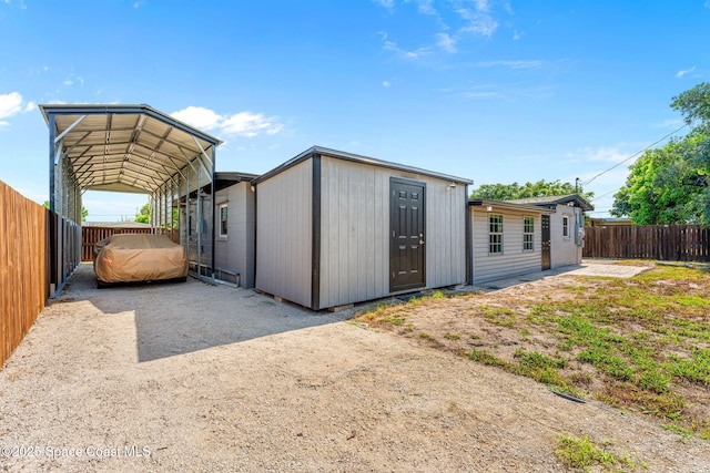 view of outbuilding featuring fence, a carport, and driveway