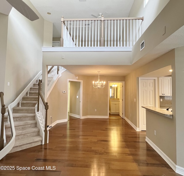unfurnished living room featuring wood finished floors, stairway, a high ceiling, a ceiling fan, and baseboards