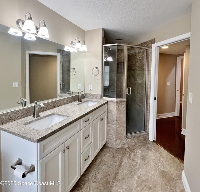 full bath featuring a textured ceiling, a stall shower, and double vanity