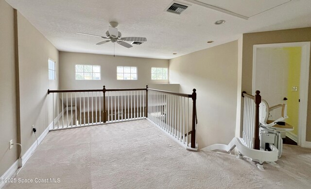 hall featuring carpet, baseboards, a textured ceiling, and an upstairs landing