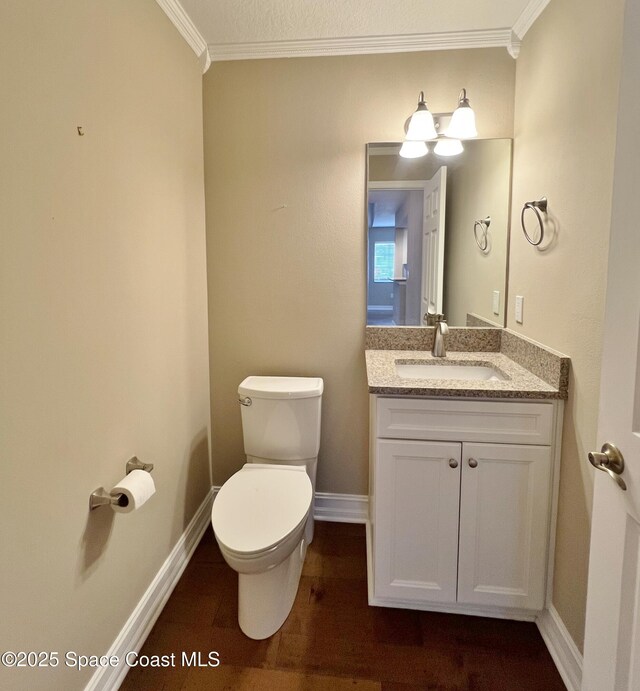 half bath with crown molding, toilet, wood finished floors, vanity, and baseboards