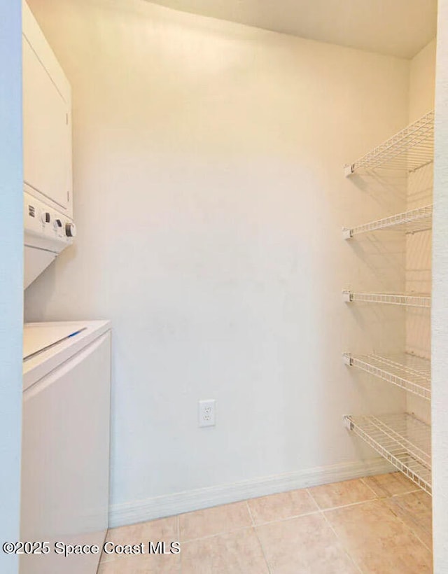 laundry room featuring stacked washing machine and dryer, baseboards, and light tile patterned floors