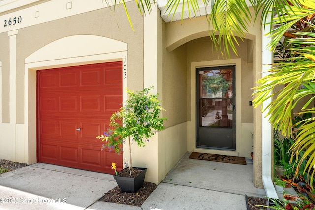 2650 Revolution St Unit 103, Melbourne, FL 32935 - view of exterior entry with stucco siding, a garage, and concrete driveway