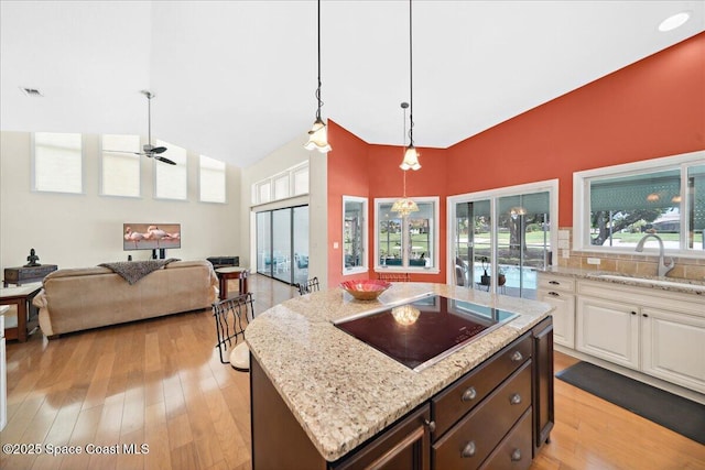 649 Spring Lake Dr, Melbourne, FL 32940 - kitchen featuring black electric stovetop, a sink, light wood-type flooring, light stone countertops, and high vaulted ceiling