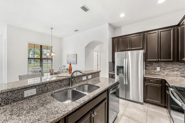 6794 Vista Hermosa Dr, Melbourne, FL 32940 - kitchen featuring stainless steel appliances, a sink, arched walkways, dark brown cabinets, and dark stone counters
