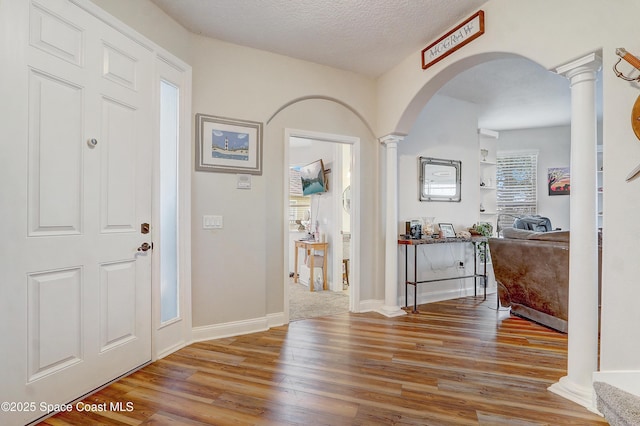 entrance foyer with decorative columns, arched walkways, wood finished floors, and baseboards