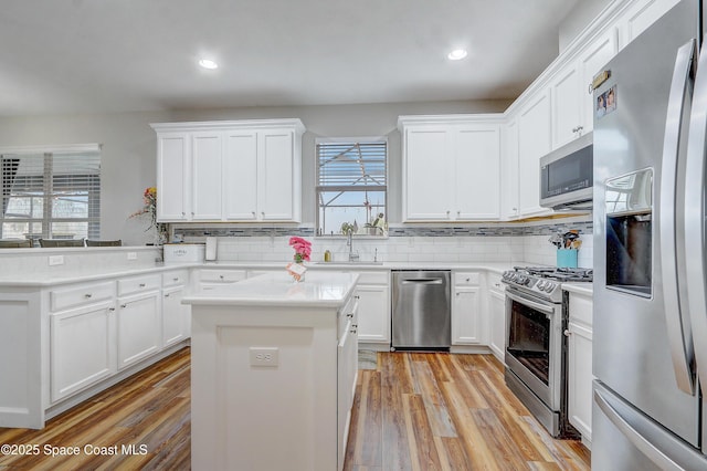 kitchen with stainless steel appliances, tasteful backsplash, light wood-style flooring, a sink, and white cabinets