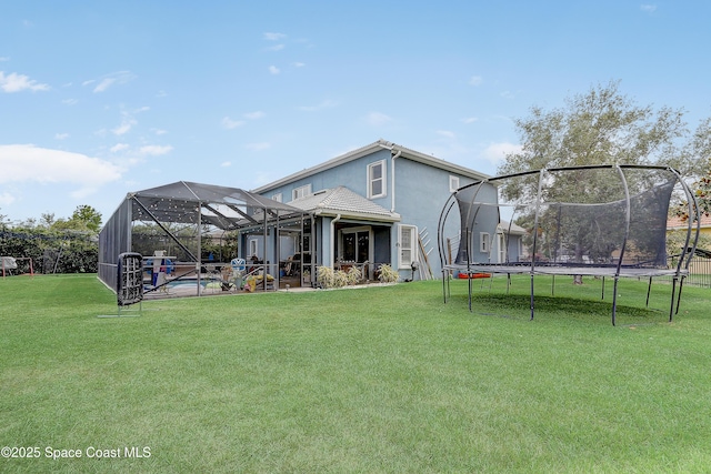 rear view of house featuring a trampoline, a yard, stucco siding, and a patio