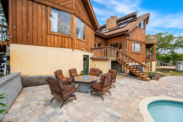 rear view of house with stairway, an outdoor fire pit, roof mounted solar panels, a patio, and a deck