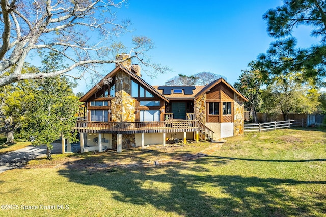 rear view of property with stone siding, a chimney, solar panels, and a deck