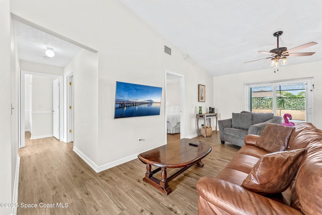 living room with light wood-type flooring, vaulted ceiling, a ceiling fan, and baseboards