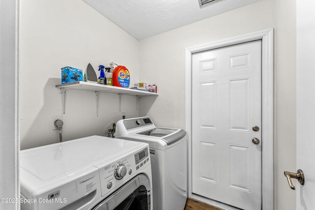 laundry area featuring washer and clothes dryer, a textured ceiling, and wood finished floors