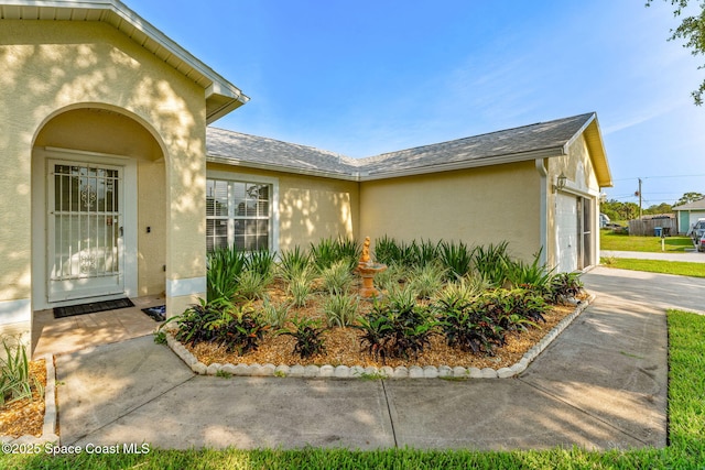 701 Agena Ave NW, Palm Bay, FL 32907 - view of exterior entry featuring stucco siding, concrete driveway, a garage, and a shingled roof