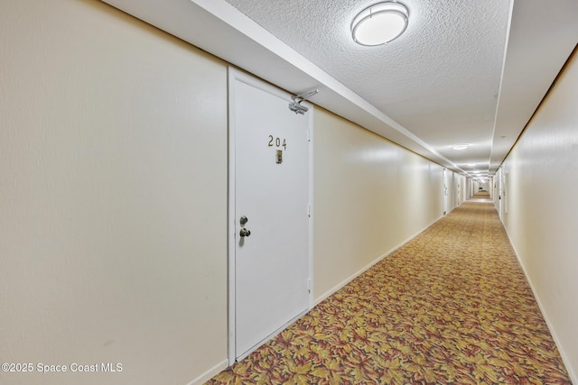 hallway with carpet, a textured ceiling, and baseboards