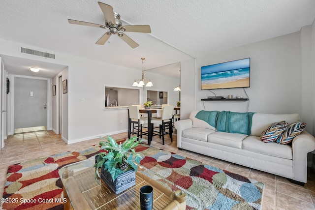 living room featuring tile patterned flooring, ceiling fan, a chandelier, a textured ceiling, and baseboards