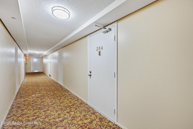 hall with a textured ceiling, light colored carpet, and baseboards