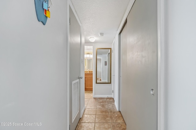 hall featuring a textured ceiling, baseboards, and light tile patterned floors
