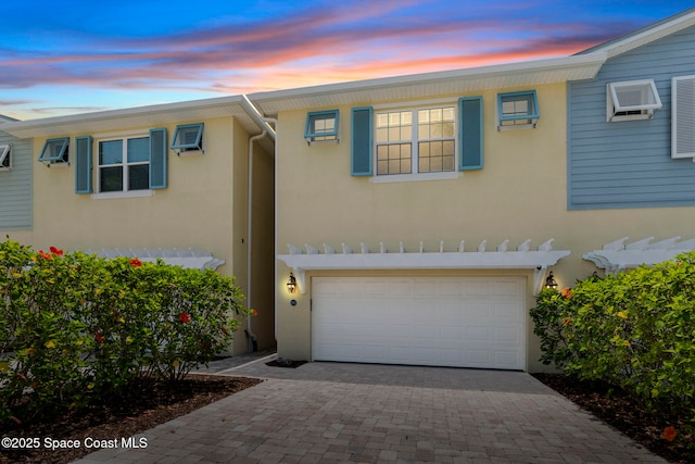 view of front of property featuring a garage, stucco siding, decorative driveway, and a wall mounted AC
