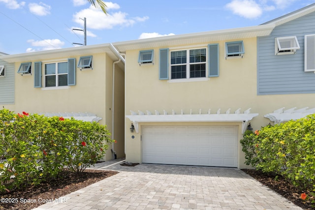townhome / multi-family property with a garage, stucco siding, decorative driveway, and a wall unit AC