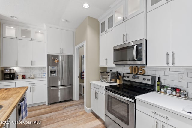 kitchen with appliances with stainless steel finishes, light wood-style flooring, backsplash, white cabinets, and recessed lighting