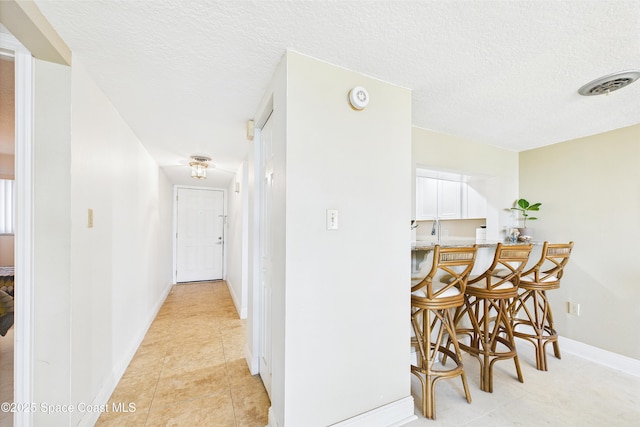 hall with light tile patterned flooring, a textured ceiling, and baseboards