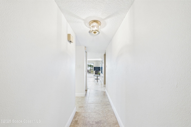 hallway featuring light tile patterned flooring, a textured ceiling, and baseboards