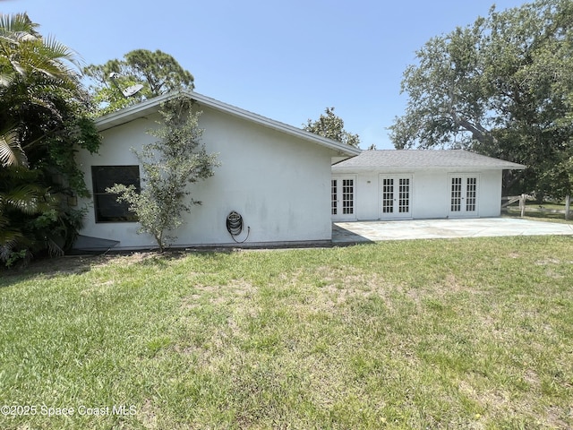 rear view of property with french doors, stucco siding, a patio area, and a lawn