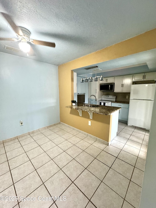 624 Ridge Club Dr Unit 86, Melbourne, FL 32934 - kitchen featuring white appliances, a peninsula, a ceiling fan, a kitchen bar, and light tile patterned flooring
