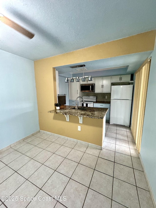 624 Ridge Club Dr Unit 86, Melbourne, FL 32934 - kitchen with white appliances, a peninsula, dark stone counters, light tile patterned flooring, and a sink