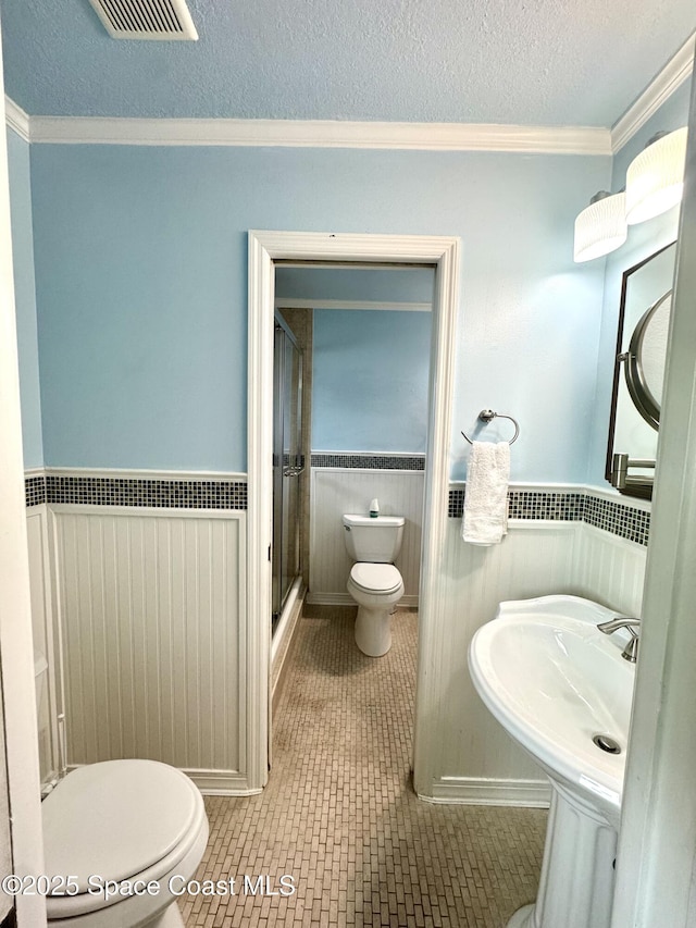 624 Ridge Club Dr Unit 86, Melbourne, FL 32934 - bathroom featuring toilet, crown molding, a shower with door, wainscoting, and a textured ceiling