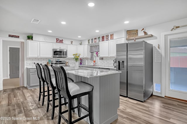 kitchen featuring stainless steel appliances, a center island, a breakfast bar, tasteful backsplash, and recessed lighting