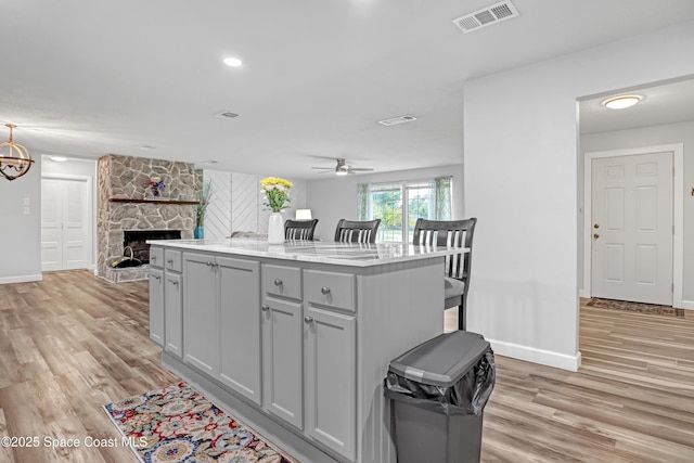 kitchen featuring light wood-style flooring, baseboards, ceiling fan, and a fireplace
