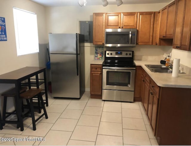 kitchen featuring stainless steel appliances, a sink, brown cabinetry, light countertops, and light tile patterned floors