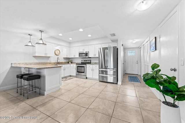 kitchen with stainless steel appliances, a peninsula, light tile patterned floors, white cabinets, and a textured ceiling