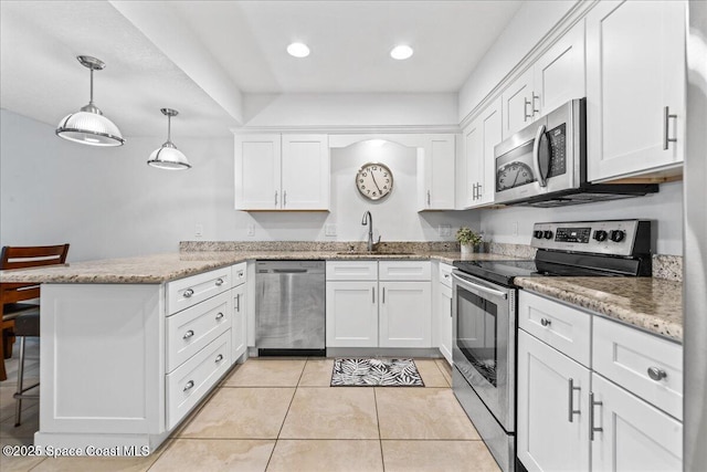 kitchen with appliances with stainless steel finishes, a sink, a peninsula, white cabinetry, and light stone counters