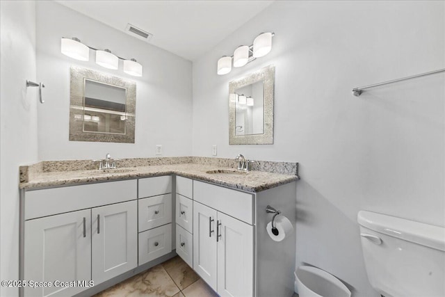 bathroom featuring toilet, double vanity, and marble finish flooring