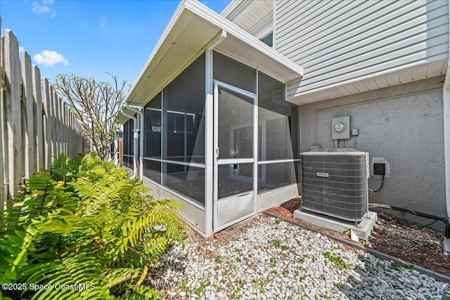 view of property exterior with cooling unit, a sunroom, and fence