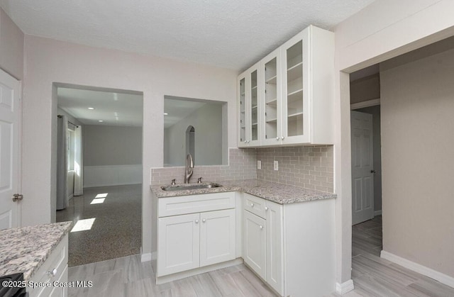kitchen with light stone countertops, glass insert cabinets, backsplash, baseboards, and a sink