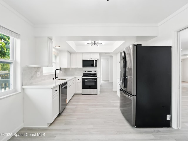 kitchen with stainless steel appliances, light wood-type flooring, a raised ceiling, a sink, and light countertops