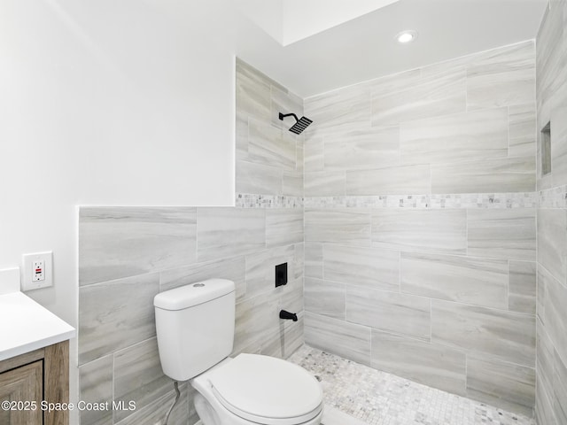 bathroom with tiled shower, toilet, vanity, and tile walls