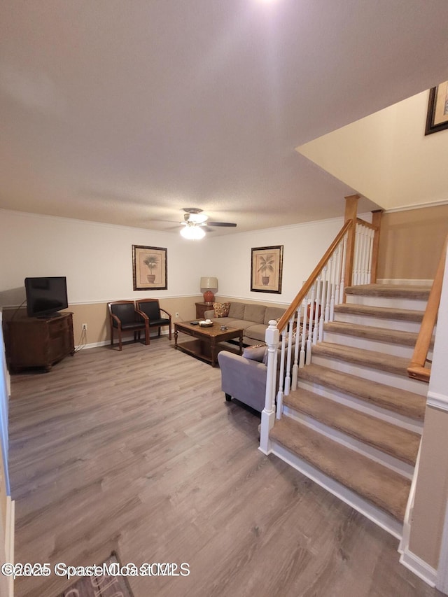 living area with stairs, wood finished floors, and ceiling fan