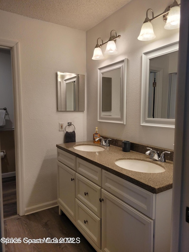 bathroom featuring a textured ceiling, double vanity, wood finished floors, and baseboards