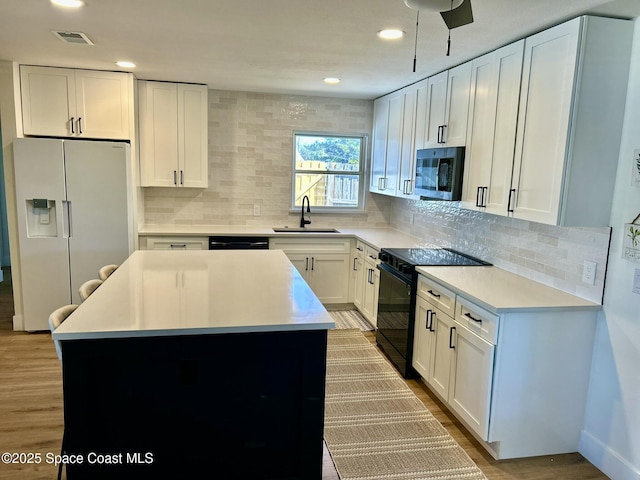 kitchen with black appliances, a sink, white cabinetry, backsplash, and recessed lighting