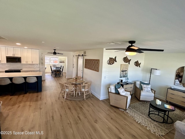 living room with ceiling fan, light wood-type flooring, baseboards, recessed lighting, and a barn door