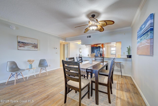 dining space featuring light wood-style floors, ornamental molding, a textured ceiling, a ceiling fan, and baseboards