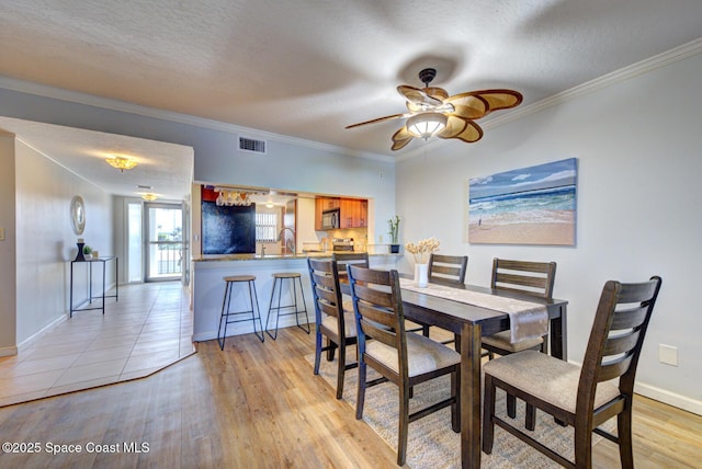 dining space with light wood-type flooring, ceiling fan, baseboards, ornamental molding, and a textured ceiling