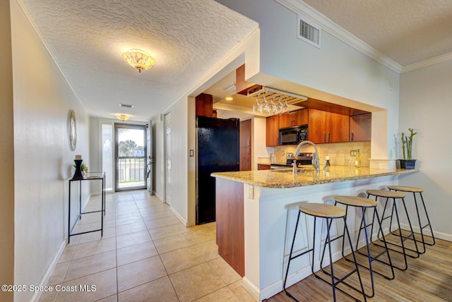 kitchen with black appliances, a peninsula, a textured ceiling, brown cabinets, and tasteful backsplash