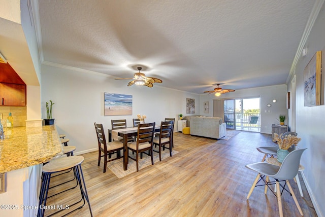 dining room with a textured ceiling, a ceiling fan, light wood-style flooring, crown molding, and baseboards
