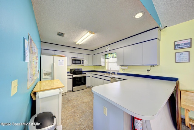 kitchen featuring stainless steel appliances, a textured ceiling, a peninsula, a sink, and white cabinetry